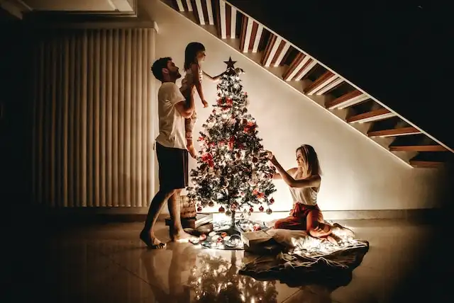 A family enjoying themselves around the Christmas tree and decorating it.